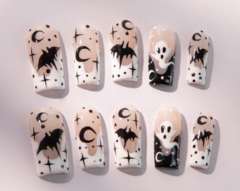 May include: A set of ten press-on nails with a Halloween theme. Each nail features a white base with black and tan designs, including bats, moons, stars, and a ghost. The nails are rectangular in shape.