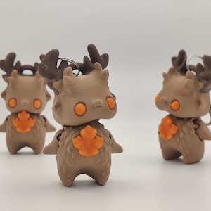 May include: Three brown figurines with deer-like antlers, orange eyes, and a leaf-shaped chest detail. The figures have small arms and are standing. The background is plain white.
