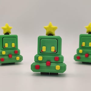 May include: Three green Christmas tree-shaped figurines with yellow star toppers. Each tree has yellow and red dot accents. The figurines are arranged in a row against a white background.