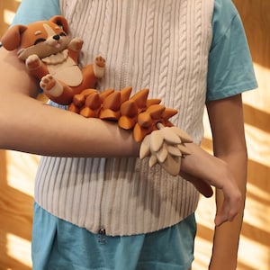 May include: A whimsical, handcrafted sculpture of a cartoon dog with a long, spiky tail. The dog is lying on its back, with its paws in the air. The sculpture is primarily orange and cream-colored.
