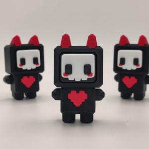 May include: Three black figurines with a pixelated heart on the chest and a skull face with red horns. The figurines have a square head and small arms and legs. The background is plain white.