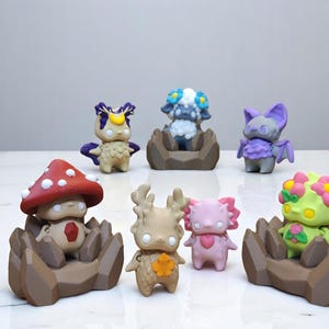 May include: Seven small, colorful, hand-painted figurines with whimsical designs. Each figurine is sitting on a brown, rocky base. The figurines include a mushroom, a deer, a bat, a flower, a sheep, and two other creatures.