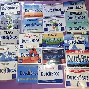 May include: A collection of Dutch Bros license plate-style magnets, each featuring a state name and design. The magnets are rectangular with the Dutch Bros logo and the number 92. States include Colorado, Arizona, and Texas.