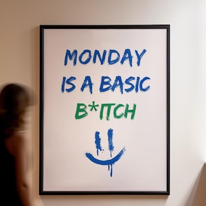 Peut inclure: Une impression encadrée avec le texte "MONDAY IS A BASIC B*TCH" en lettres bleues et vertes. Un smiley bleu avec de la peinture qui coule se trouve sous le texte.