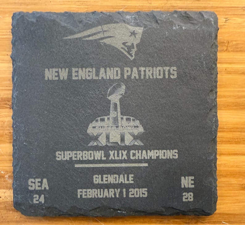 May include: A black slate plaque with the words "New England Patriots" and "Super Bowl XLIX Champions" engraved on it. The plaque also includes the date "February 1 2015" and the scores "SEA 24" and "NE 28".