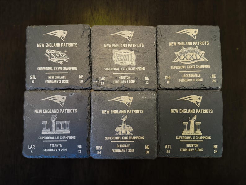 May include: Six black slate coasters with white text and images commemorating the New England Patriots Super Bowl wins. Each coaster features the team logo, the Super Bowl number, the year, and the opponent city.