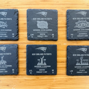 May include: Six black slate coasters with the New England Patriots logo and Super Bowl winning information. Each coaster features the year, Super Bowl number, opponent, score, city, and date of the win.