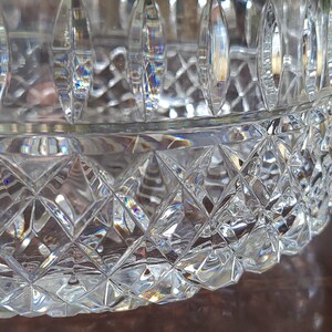 Puede incluir: Un cuenco de cristal tallado transparente con un patr&oacute;n de diamantes y cortes verticales. El cuenco es redondo con una abertura ancha y se asienta sobre una superficie marr&oacute;n. El cristal refleja la luz, creando un efecto brillante. Una pieza decorativa.