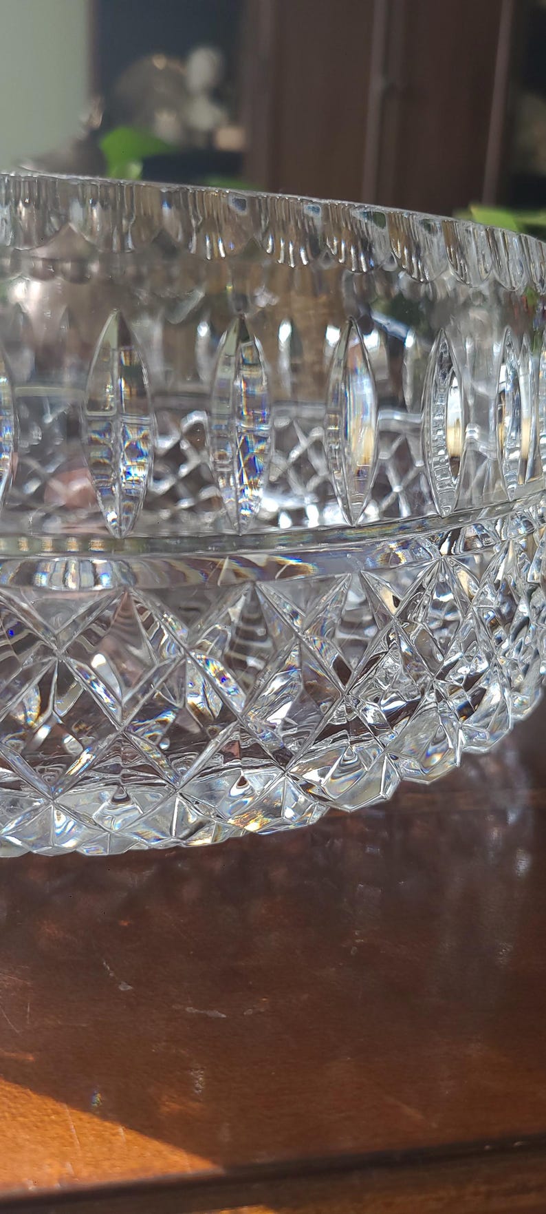 Puede incluir: Un cuenco de cristal tallado transparente con un patr&oacute;n de diamantes y cortes verticales. El cuenco es redondo con una abertura ancha y se asienta sobre una superficie marr&oacute;n. El cristal refleja la luz, creando un efecto brillante. Una pieza decorativa.