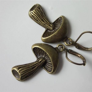 May include: A pair of bronze mushroom-shaped earrings with a hook closure. The earrings are detailed with a textured surface and a raised mushroom cap.