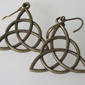 May include: A pair of bronze-colored earrings featuring a Celtic knot design. Each earring has a triangular shape with interwoven lines, and a hook for pierced ears. The earrings are displayed against a white background.