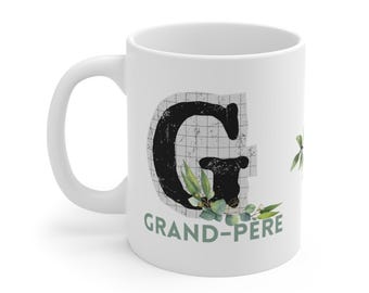 May include: White ceramic mug with a large black letter "G" and the words "GRAND-PERE" in green. The letter is decorated with a grid pattern and green leaves.
