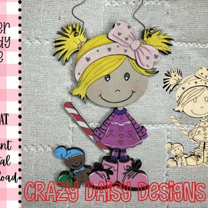 May include: A whimsical wooden ornament featuring a girl with yellow hair, a pink bow, and a purple dress, holding a candy cane. A gingerbread man and another girl are also present. The words "CRAZY DAISY DESIGNS AZ" are at the bottom.