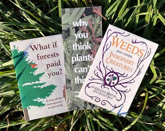 May include: Three zines with botanical themes are displayed on a bed of green grass. The zines feature text such as "What if forests paid you?" and "Weeds and Other Imaginary Creatures." The zines are in shades of green, white, and orange.