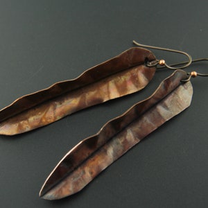 May include: A pair of long, copper earrings shaped like leaves. The earrings have a textured, hammered finish and are suspended from simple wire hooks.
