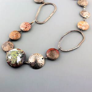 May include: A handcrafted necklace featuring large, round, fossilized stone beads in shades of brown, orange, and green. The necklace is accented with hammered silver-tone metal discs and oval links, creating a unique and earthy design.