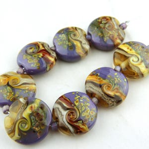 May include: A bracelet composed of seven round, flat glass beads. Each bead features a swirling pattern of purple, amber, and cream colours with small gold-toned flecks embedded within the glass. The beads are connected by small, light purple spacers.