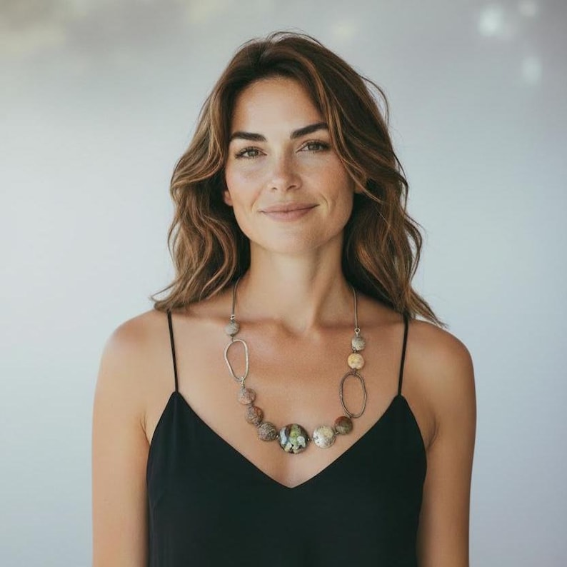 May include: A silver-toned necklace with a variety of natural stone beads and oval accents. The necklace features a large, round central stone and is worn with a black spaghetti strap top.