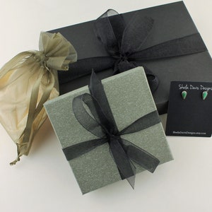 May include: Gift boxes and jewelry packaging. A black box and a gray box are tied with black ribbon. A small pair of green teardrop earrings on a black card. A small beige organza gift bag.