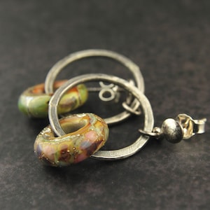 May include: Silver hoop earrings with two colorful glass beads. The beads are round and have a speckled pattern in shades of green, brown, and pink.