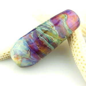May include: A cylindrical glass bead featuring a swirling, marbled pattern of purple, orange, blue, and pale green hues. The surface is smooth and glossy, with small internal air bubbles visible throughout the translucent, multi-colored glass material.