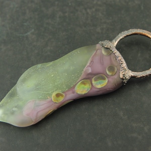May include: A green and purple glass pendant with iridescent bubbles, attached to a copper wire loop.