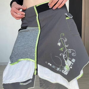 May include: A grey wrap skirt with a distinctive design. The skirt combines grey, white, and black fabrics, highlighted with neon green trim. It has an asymmetrical hemline and decorative embroidery.