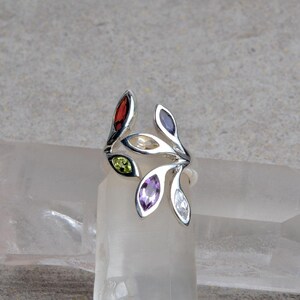 May include: A silver ring with a leaf design featuring five gemstones: red, yellow, green, purple, and white.