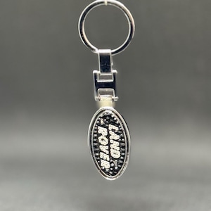 May include: Silver key ring with a black oval charm that says "LAND ROVER" in white letters.