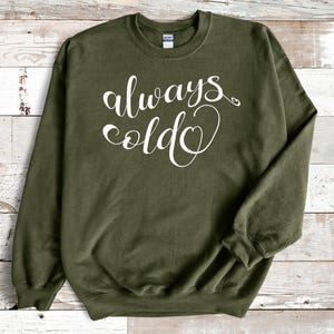 May include: A green sweatshirt with the text "always cold" in white lettering with a heart symbol.