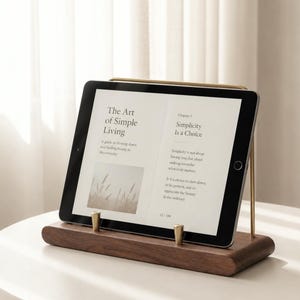 Peut inclure: Une tablette numérique posée sur un support en bois foncé doté de deux petites chevilles en laiton. L'écran affiche le texte The Art of Simple Living et Chapter 1 Simplicity Is a Choice, avec une image d'herbes hautes dans un champ.