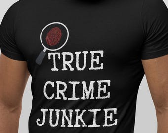 Op de afbeelding: Zwart T-shirt met de witte tekst "TRUE CRIME JUNKIE" en een vergrootglas met een rode vingerafdruk. Het T-shirt heeft een ronde hals.