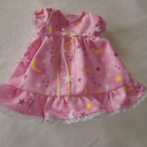May include: A pink nightgown with a yellow ribbon tie and a white lace trim. The fabric has a pattern of yellow stars and crescent moons on a pink background.