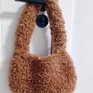 A brown curly teddy fleece handbag hanging on a black door handle against a white door.