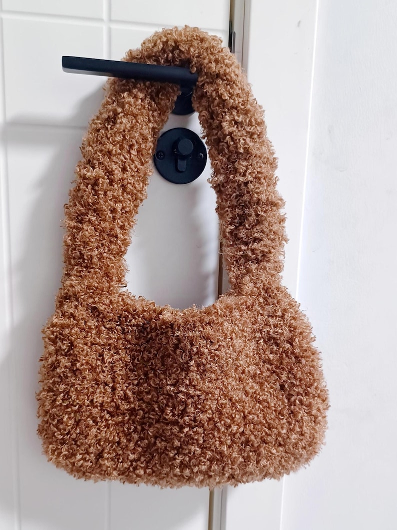 A brown curly teddy fleece handbag hanging on a black door handle against a white door.