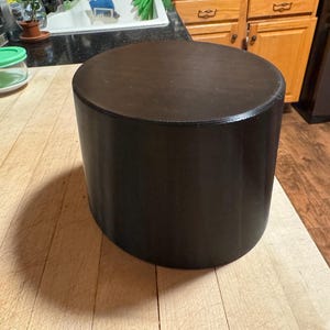 May include: A dark brown wooden chopping board with a smooth surface. The board is round and has a slightly raised edge.