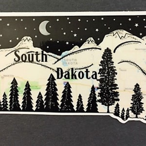 May include: A South Dakota-shaped sticker with a black and white illustration. The design shows a night sky with stars and a crescent moon, mountains, and pine trees. The words "South Dakota" are written across the center of the sticker.