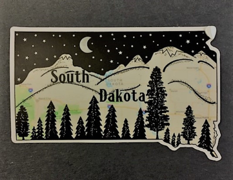 May include: A South Dakota-shaped sticker with a black and white illustration. It depicts a night sky with stars and a crescent moon, a mountain range, and pine trees. The state's name is written across the center.