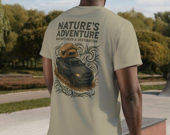 以下が含まれることがあります： 「Nature's Adventure Doesn't Need a Destination」の文字とトラックのイラストがプリントされたベージュ色のTシャツ。人物は薄いブルーのジーンズとグレーのバケットハットを着用しています。背景はスケートパークです。