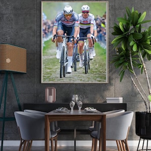 Puede incluir: Una impresión enmarcada de una carrera ciclista. Dos ciclistas en primer plano, con cascos, montan en bicicleta por una carretera adoquinada. El fondo muestra espectadores, con los ciclistas en movimiento.