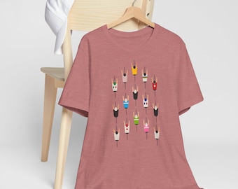 Op de afbeelding: Een heidekleurig rood T-shirt met een afbeelding van een groep fietsers in verschillende gekleurde truien. De fietsers rijden in een rij, met hun rug naar de kijker.