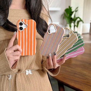 Puede incluir: Una colección de fundas de teléfono coloridas con bordes ondulados. Una funda es naranja con rayas verticales blancas. Otras fundas presentan rayas pastel en varios colores, incluyendo rosa, verde y amarillo. Las fundas están diseñadas para un smartphone.