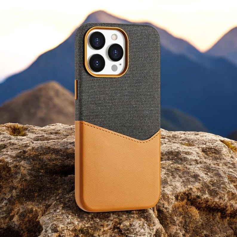 May include: A gray and brown phone case with a textured fabric exterior and a leather-like flap. The case has a raised camera bump with three lenses.
