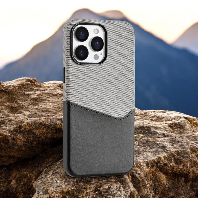 May include: A gray and black phone case with a textured fabric exterior and a black leather-like pocket on the back.
