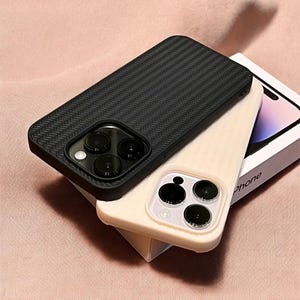 Op de afbeelding: Twee telefoonhoesjes, een zwarte met een textuurpatroon en een beige. Beide hoesjes hebben een verhoogd cameragebied met drie ronde uitsparingen.