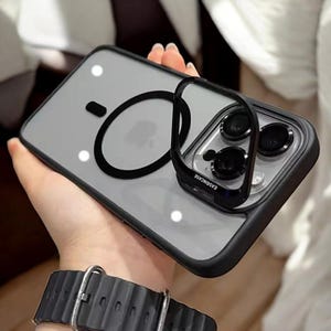 Op de afbeelding: Een transparante telefoonhoes met een zwarte ringhouder en een zwarte camera lensbeschermer. De hoes heeft een verhoogde rand rond de camera lenzen en een transparante achterkant. De tekst "EASYCASE" is gedrukt op de camera lensbeschermer.