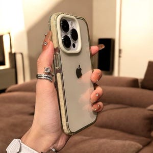 Op de afbeelding: Een transparante telefoonhoes met een verhoogde camerabult en een witte rand. De hoes is ontworpen voor een iPhone met een transparante achterkant en een wit Apple-logo.
