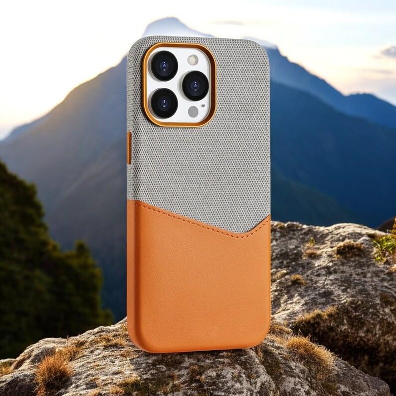 May include: A gray and orange phone case with a textured fabric exterior and a smooth leather-like bottom. The case has a cutout for the phone's camera lenses.