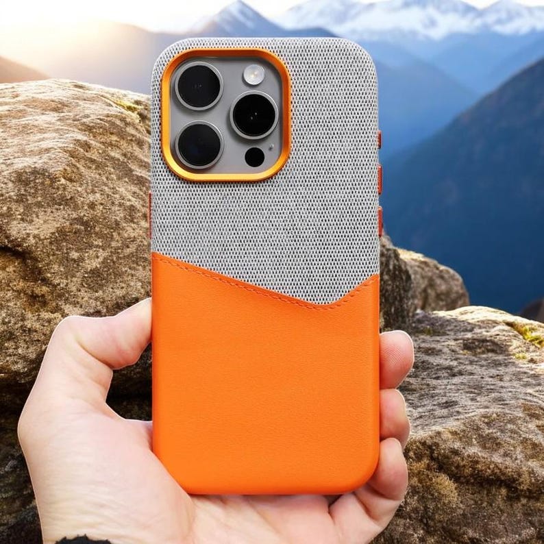 May include: A gray and orange phone case with a textured fabric exterior and a smooth leather interior. The case has a cutout for the camera lens.