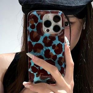 Könnte beinhalten: Transparente Handyhülle mit Leopardenmuster in Braun- und Blautönen. Die Hülle hat eine glänzende Oberfläche und ist für ein Smartphone konzipiert. Das Wort "Leopard" ist auf der Hülle aufgedruckt.